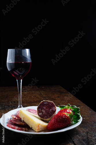 Piatto Fontina, salame, fragole e vino rosso sfondo nero photo