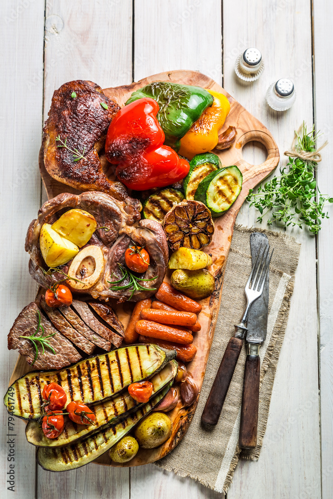 Roasted steak and vegetables with herbs on white table