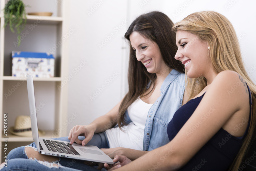 two women using laptop and smiling on sofa in her home