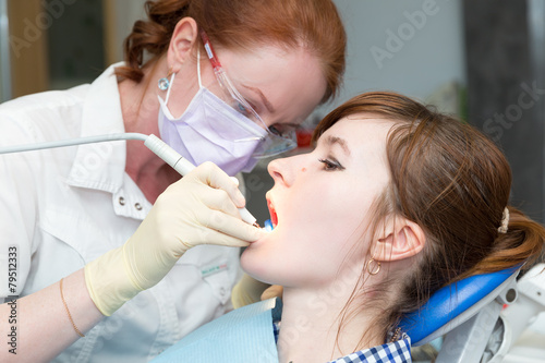 Dentist with glasses and mask treats teeth of girl