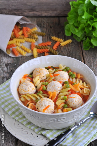 soup with meatballs, pasta, peas and parsley on a wood table