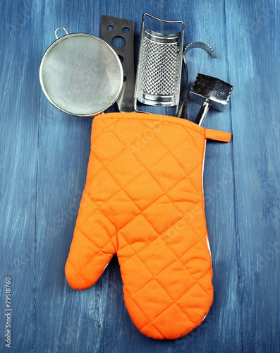 Different kitchen utensils in potholder on wooden background photo