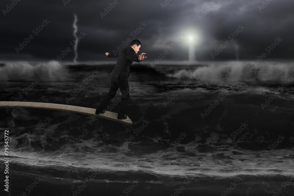 Businessman balancing on wooden board with dark stormy ocean Businessman balancing on wooden board with dark stormy ocean
