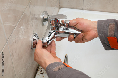 Plumber works in a bathroom replacing faucet, tap