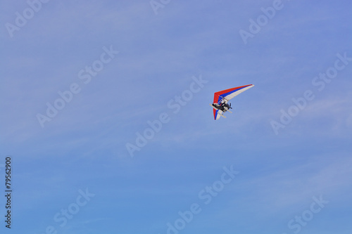 The hang-glider flying against a blue sky with clouds