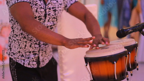Young male percussionist playing cuban drums against black