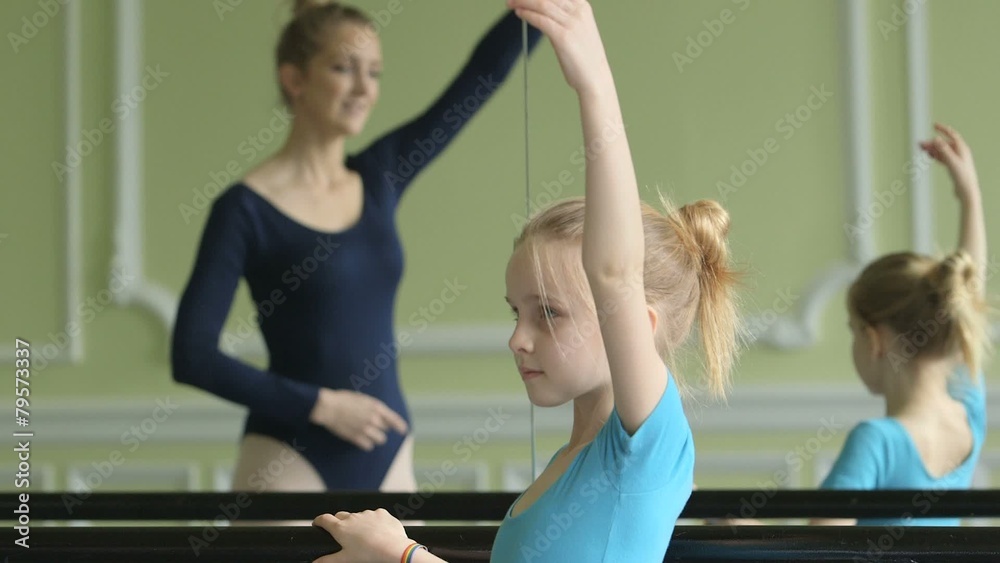 Female Baller Dancer in background instructs younger Ballerina on her movement as she poses in the foreground Female Baller Dancer in background instructs younger Ballerina on her movement as she poses in the foreground