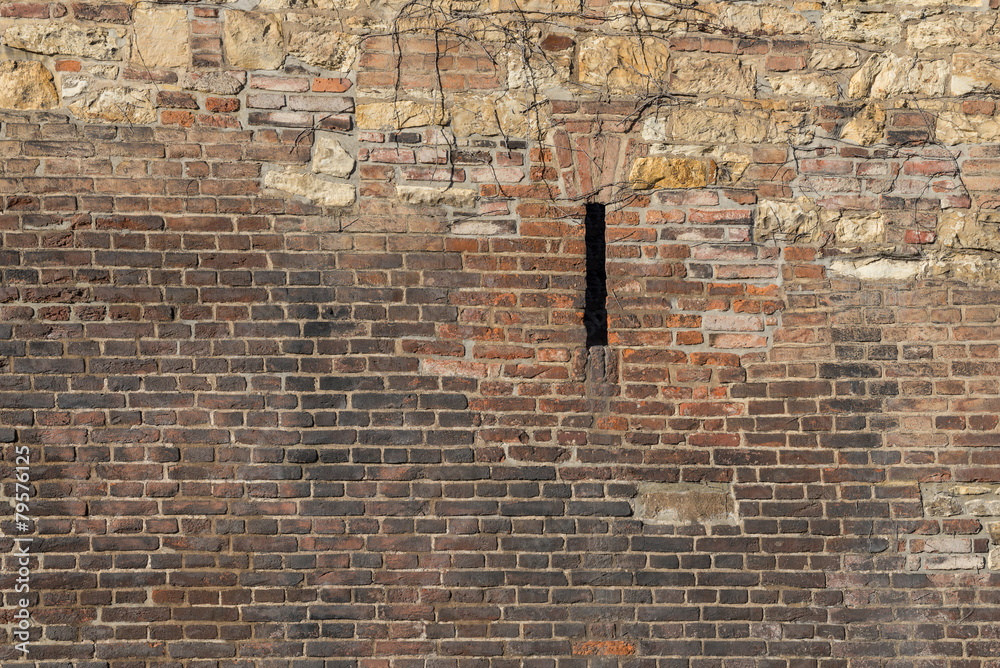 Old brick wall with wild stone and a narrow porthole Old brick wall with wild stone and a narrow porthole