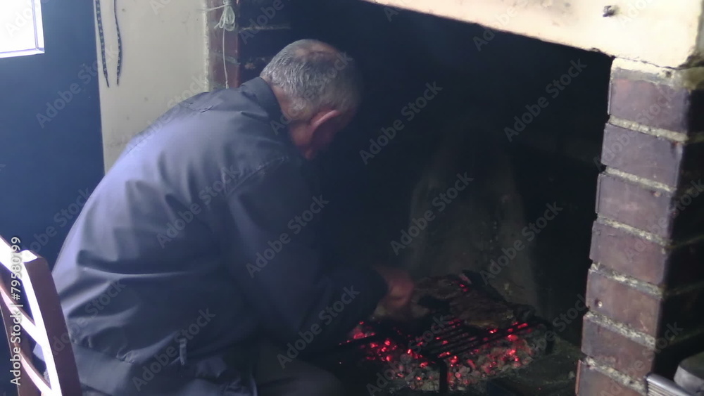 old man cooks steaks on the grill in front of a fireplace old man cooks steaks on the grill in front of a fireplace