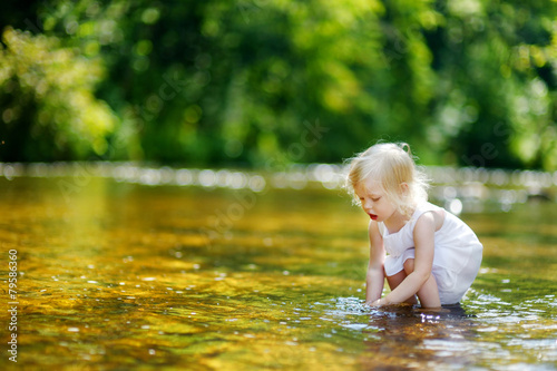 Fototapeta Naklejka Na Ścianę i Meble -  Cute little toddler girl having fun by a river