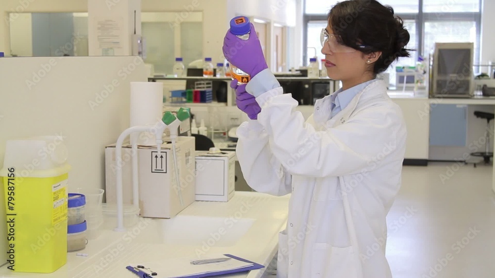 Scientist looking at liquid in laboratory and making notes Scientist looking at liquid in laboratory and making notes