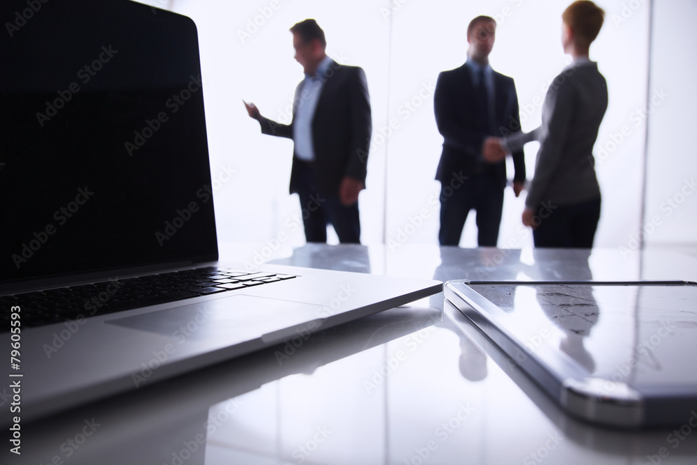 Laptop  computer on  desk , three businesspeople standing in the