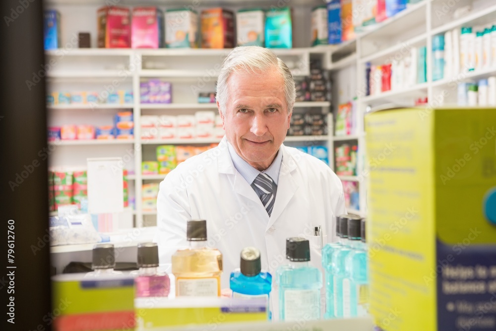 Smiling senior pharmacist standing behind a shelf