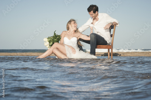 Young beautiful couple sitting at water's edge flirting in love