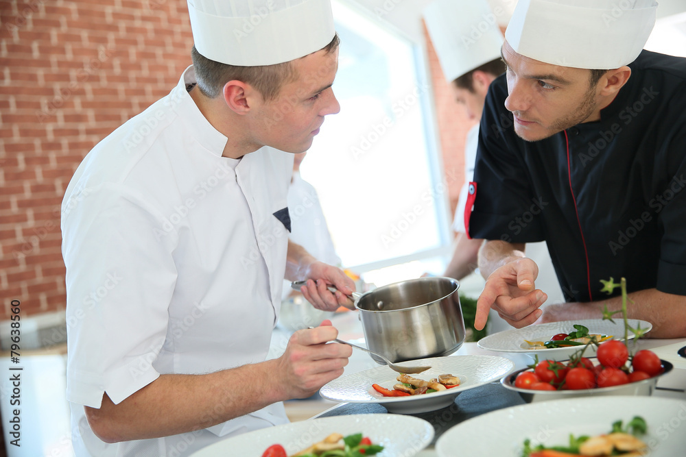 Chef with young cook in kitchen preparing dish Chef with young cook in kitchen preparing dish