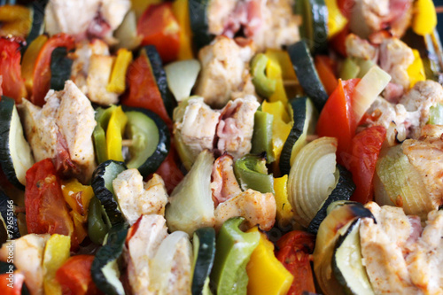 Close-up of chicken skewers with bacon and vegetables on a tray.