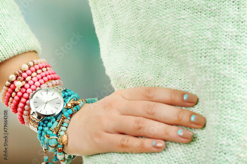 Stylish bracelets and clock on female hand close-up
