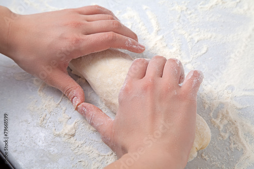 Woman's hands knead dough on a table with flour