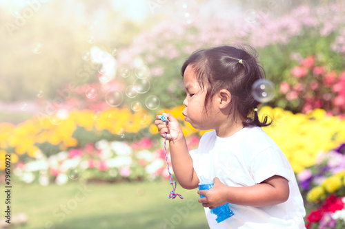 Cute little girl is blowing soap bubbles in flower garden in vin