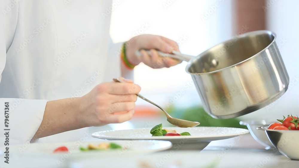 Closeup of woman in restaurant kitchen pouring sauce 