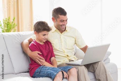 Happy father and son using laptop on sofa