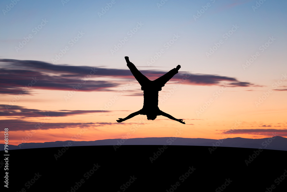 silhouetted young man jumping upside down in sunset