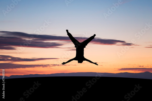 silhouetted young man jumping upside down in sunset