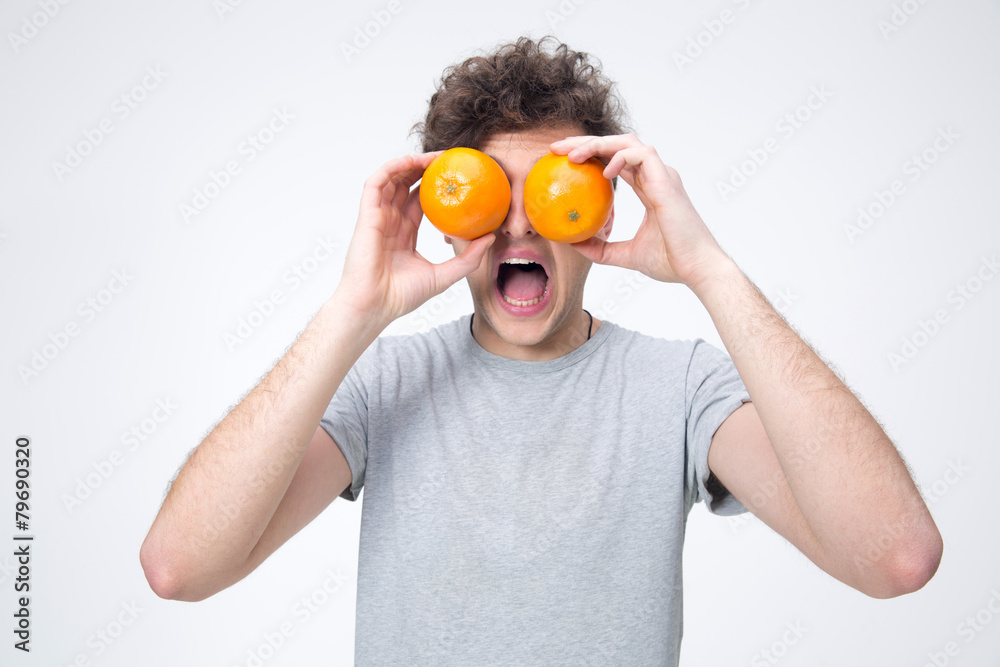 Surprised man looking through oranges over gray background Surprised man looking through oranges over gray background