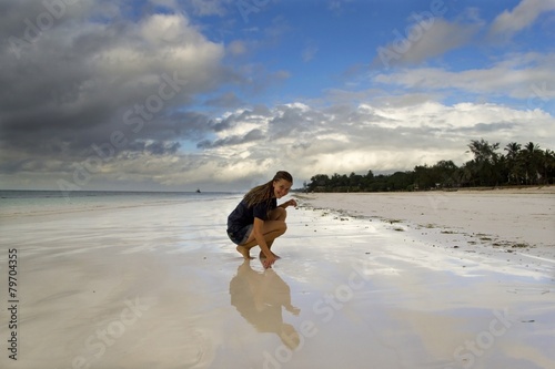 Young woman sitting on beach with reflective sand