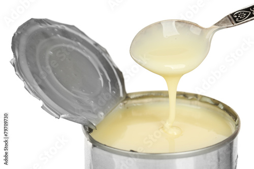 Tin can of condensed milk with spoon isolated on white