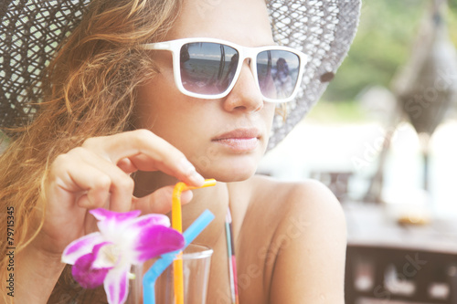 Beautiful young woman in sunglasses with a cocktail at the bea