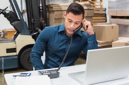 Warehouse manager using telephone and laptop