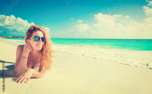 Smiling beautiful woman with sunglasses sunbathing on a beach