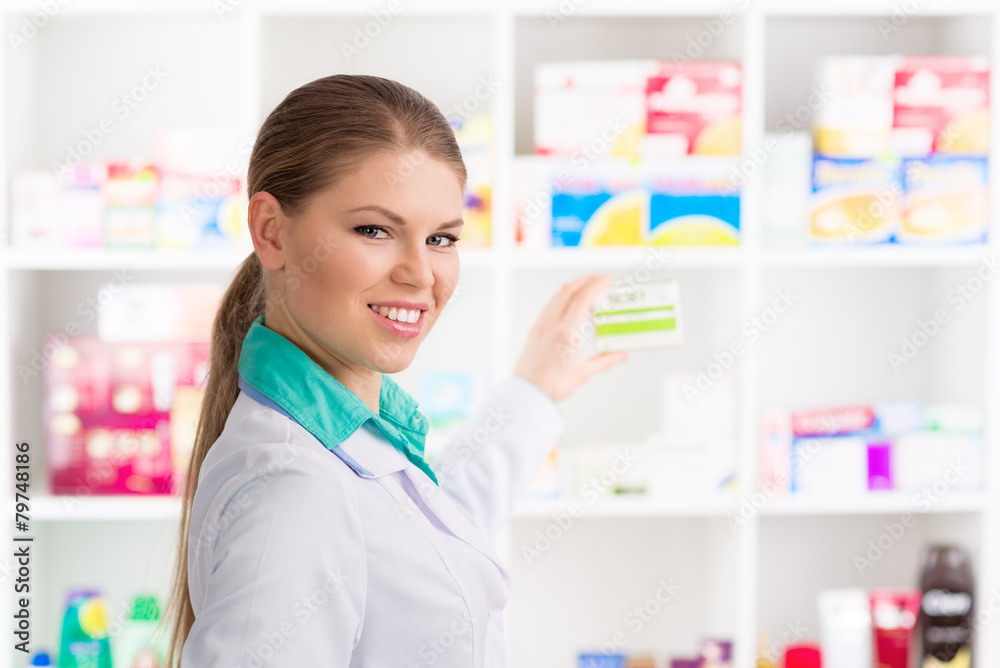 Friendly female pharmacist taking medicine box from the shelf