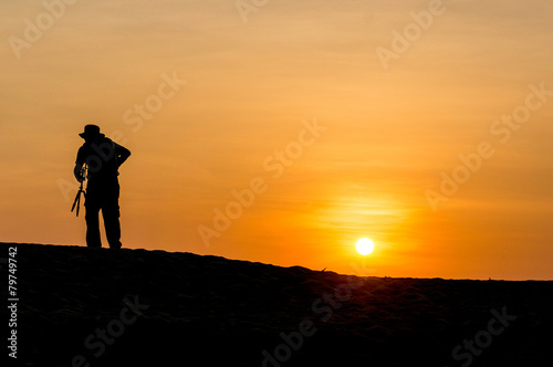 Man in silhouette holding a tripod walking at tropical beach