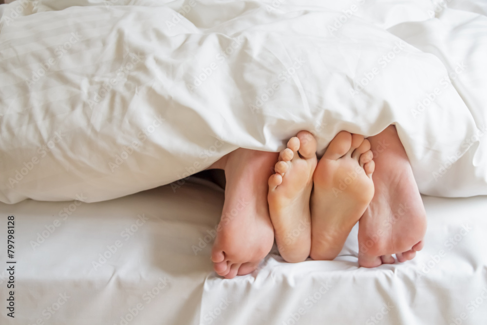 Two pairs of feet under the covers at home in bedroom Two pairs of feet under the covers at home in bedroom