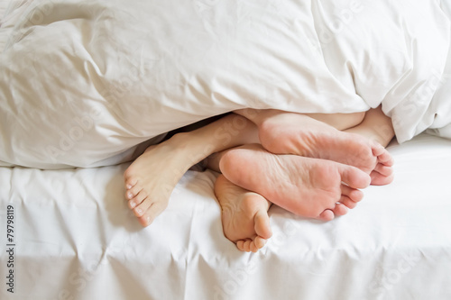 Two pairs of feet under the covers at home in bedroom