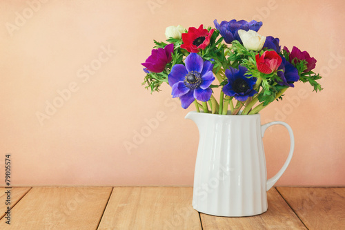 Anemone flowers in white vase on wooden table