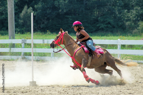 Teenage girl on horseback races around a pole