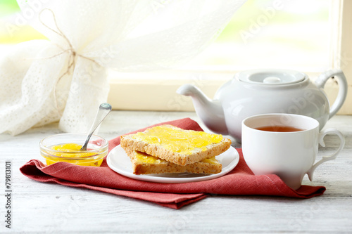 Toasts with honey on plate and cup of tea on light background