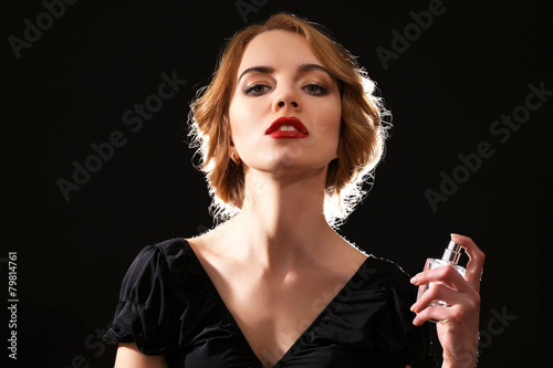 Beautiful young woman with perfume bottle on black background