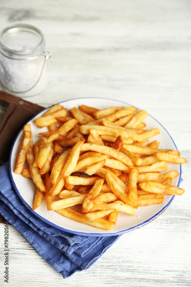 Tasty french fries on plate, on wooden table background Tasty french fries on plate, on wooden table background