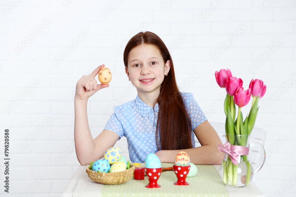 Cute girl decorates Easter eggs, on light background Cute girl decorates Easter eggs, on light background