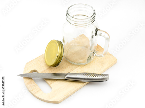 An empty jar with the cap and knife on wood board