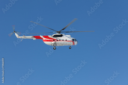 Red and white helicopter flying in the blue sky
