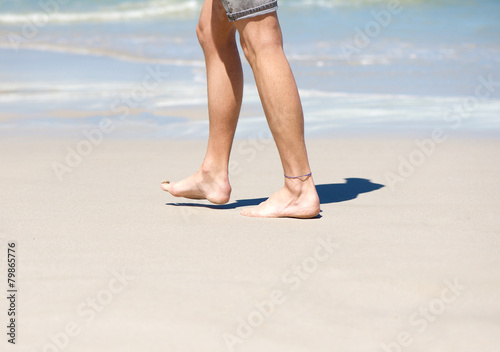 Man walking barefoot on white sand beach