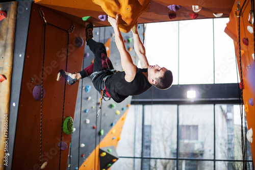 Young man practicing rock-climbing in indoor climbing gym