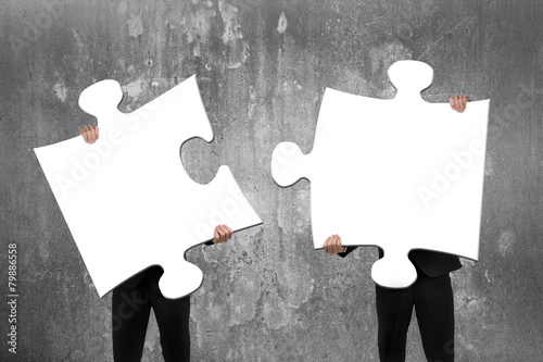 Two business people assembling white jigsaw puzzles with concret photo