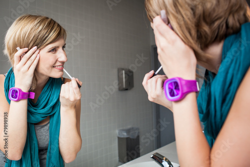 Pretty, young woman applying mascara /eyeshadows in front of a m