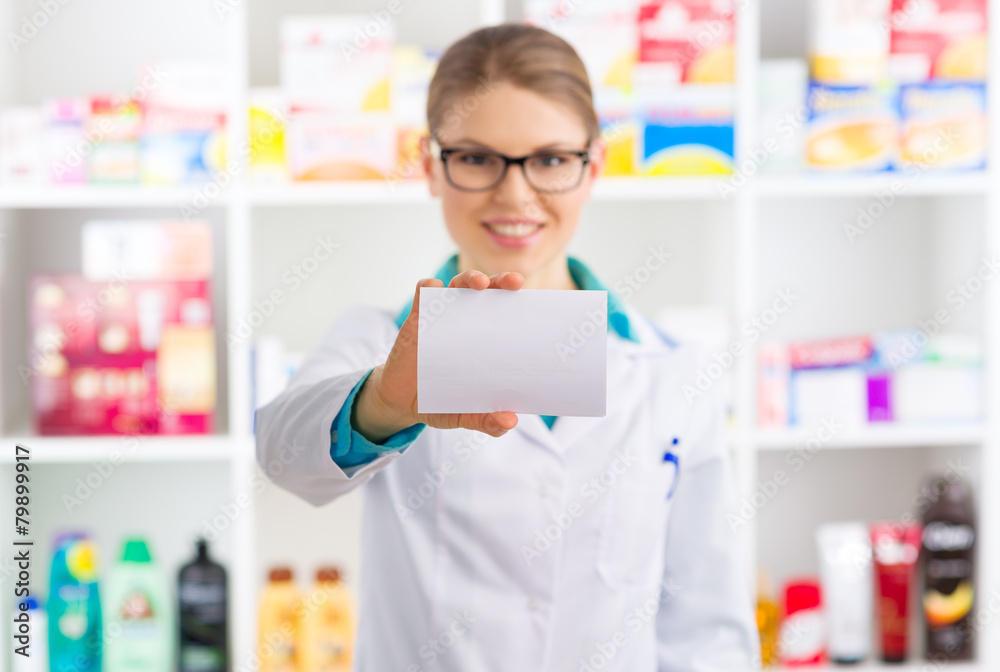 Smiling pharmacist showing blank paper over shelves background